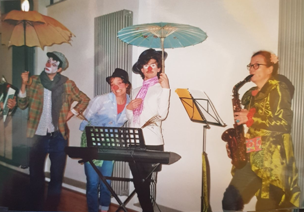 4 Clowns mit Regenschirm und Instrumenten auf einer Bühne.